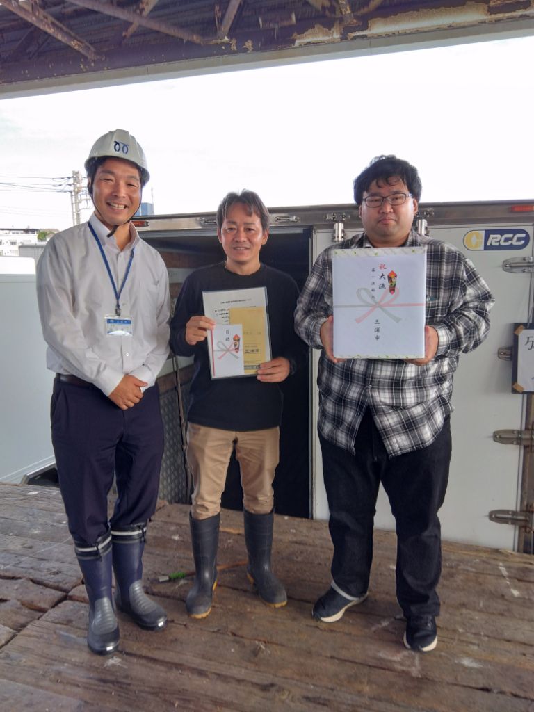 男性3人が並んで記念品を持っている写真