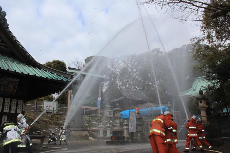 神社で消防団員が複数人でホースから放水し火事を想定した訓練をしている様子の写真