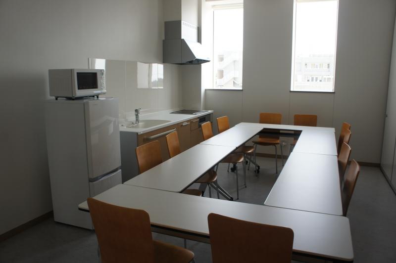 四角に囲んだテーブルに椅子が12個あり冷蔵庫、電子レンジ、流し台が完備された中規模の研修室の写真