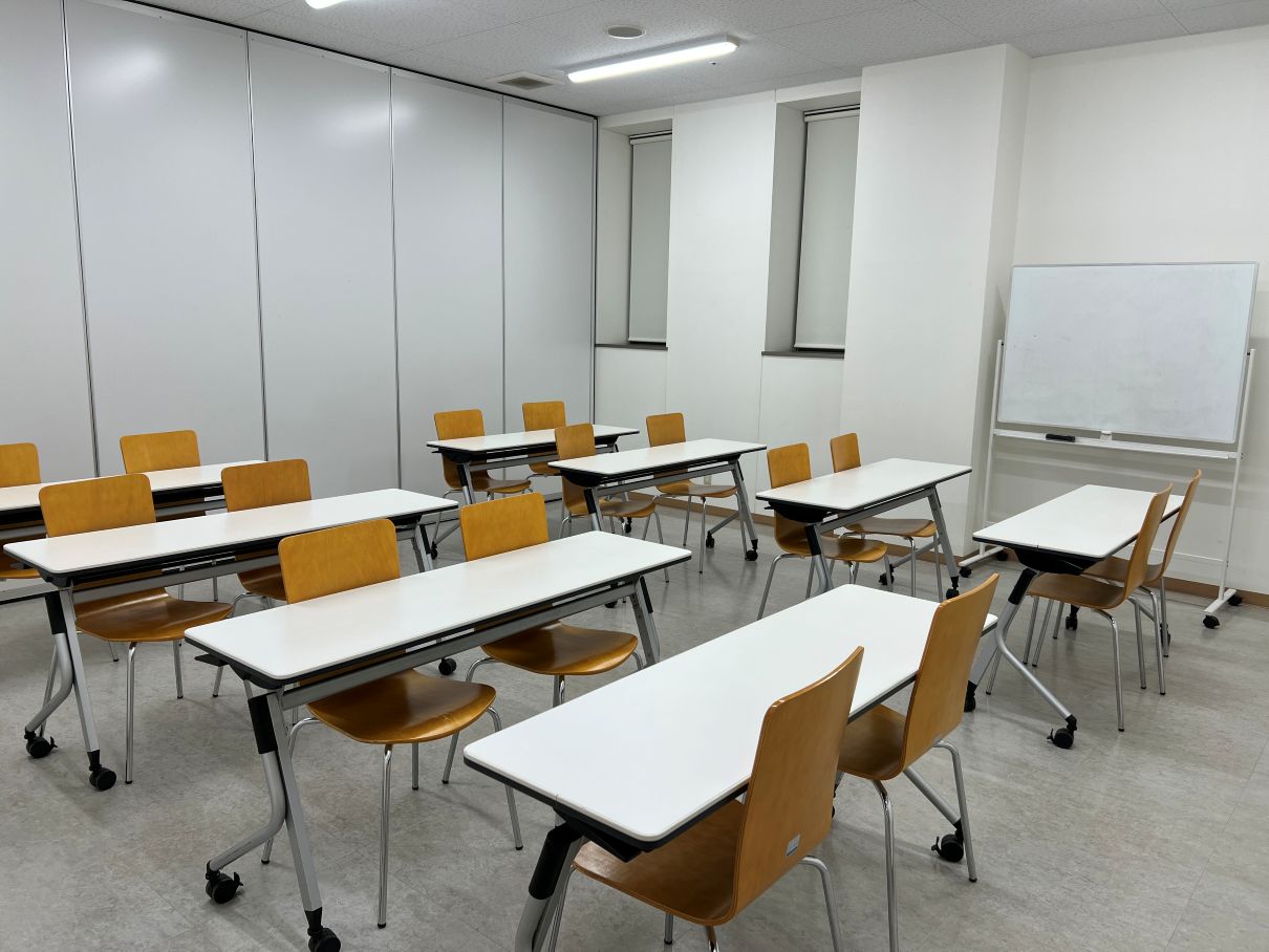 並んだテーブルに椅子が16個ある大きな研修室の写真