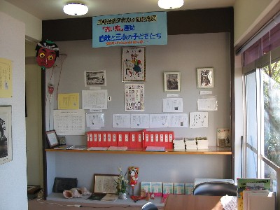 「白秋と三小の子どもたち」と書かれた張り紙の下に、写真や紙の資料が展示され、その下に赤い背表紙の本が並んでいる写真