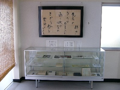 文献や写真資料が展示されているガラスケースの上に、詩が書かれた文書が入っている額縁が飾られている写真