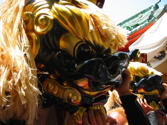 沢山の人々が持ち上げている獅子舞の顔部分をアップに写した写真