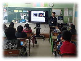 教室内でモニターを用いて授業を行う東京大学三崎臨海実験所の職員と、着席し話を聞く児童らの写真