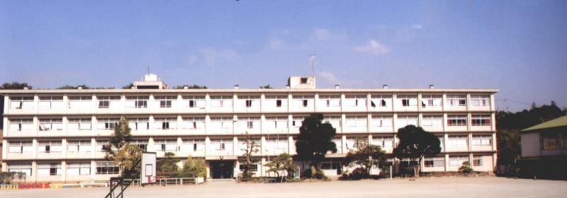 白い校舎の前にバスケットゴールや鉄棒が設置された校庭がある上宮田小学校の写真