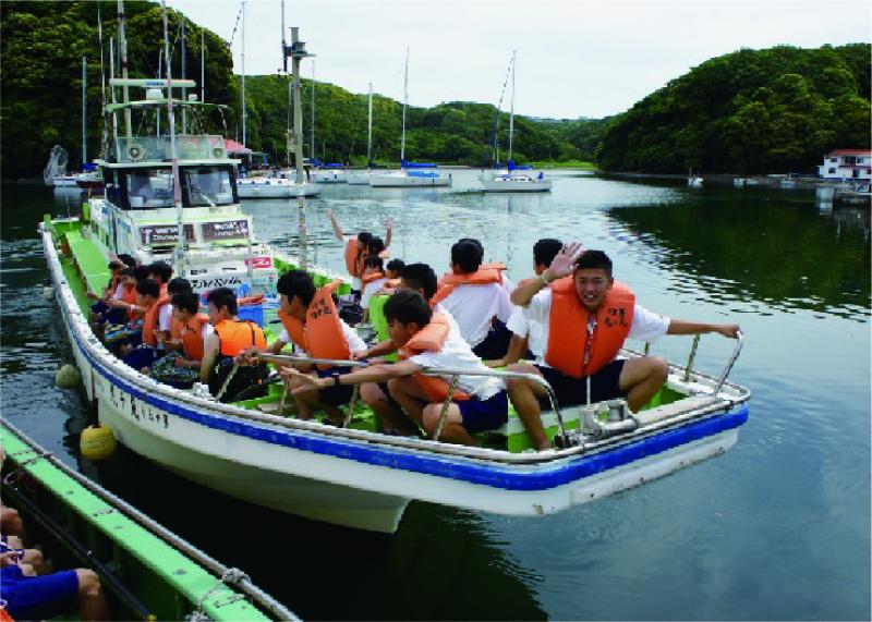 オレンジ色の救命胴衣を身に着けた生徒たちが、漁船に乗り込んでいる写真