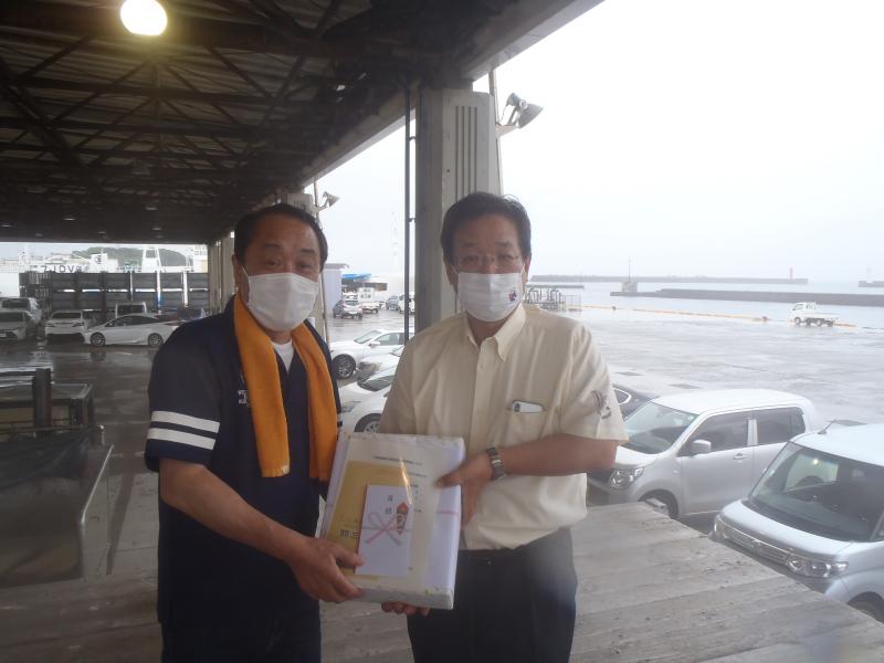 オレンジのタオルを首にかけた第151勝運丸船主と、クリーム色のワイシャツを着た三浦市長が記念品を持って並んでいる写真