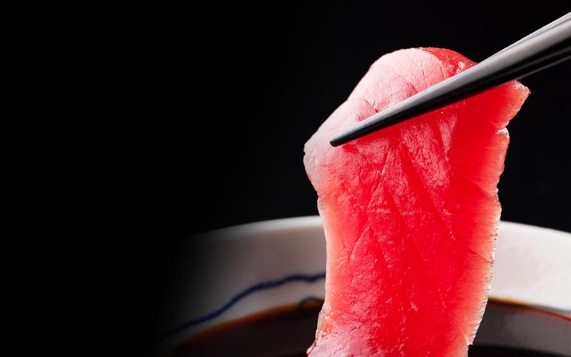 A Photo of a sliced raw maguro dipped in soy sauce and lifting up by chopsticks