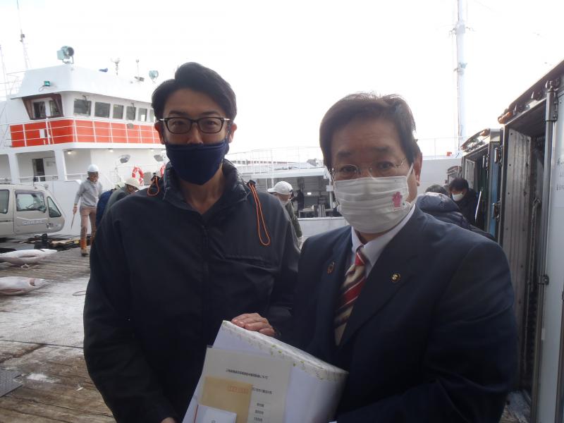 黒縁の眼鏡をかけた池田水産株式会社専務と、スーツ姿の三浦市長が、漁船を後ろに並んで写っている写真
