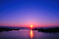 雲一つない夕空と海の水平線の上に太陽が見えている写真