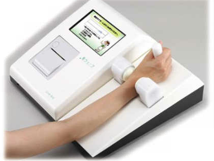 白い色で左側にモニターと測定結果の印刷機が右側に腕を置く場所がある測定器に手首を挟み計測している様子の写真