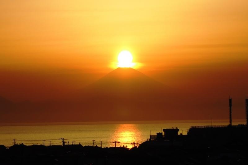 手前に広がる湖から見て夕日が富士山山頂に重なった瞬間の写真