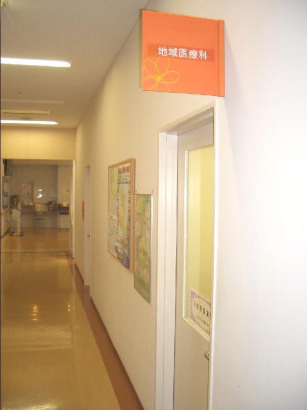 奥へ伸びる白壁の廊下と地域医療科のオレンジ色の案内板の下にある扉の写真