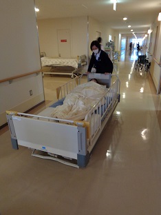 廊下で柵のついた大きなベッドを動かしている女性の写真