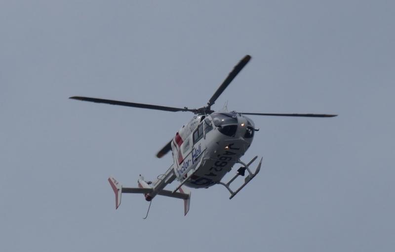 白に赤いラインと青い文字の入ったボディに黒いプロペラのヘリコプターが上空を飛んでいる写真