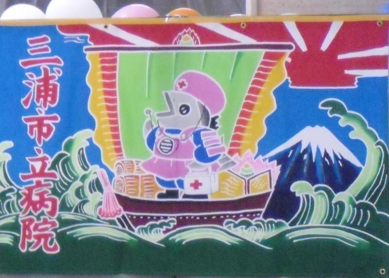 「三浦市立病院」と書かれた、宝船に乗った看護師姿のマグロのイラストの横断幕の写真