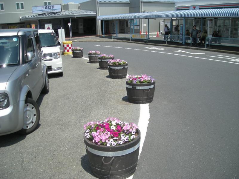 車を誘導するために置かれている樽型の花壇に白色やピンク色、赤色の花が植えられている写真