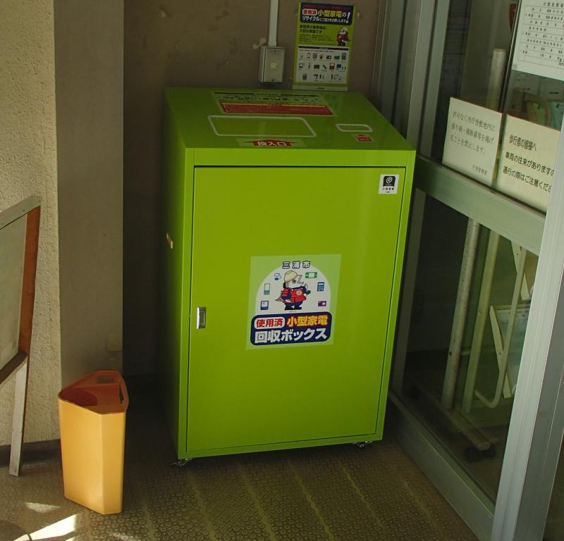 建物の入り口に黄緑色の小型家電回収ボックスが設置されている様子の写真