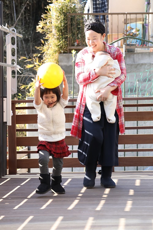 黄色いボールを頭に載せて遊ぶ娘と、子どもを抱っこする母の写真