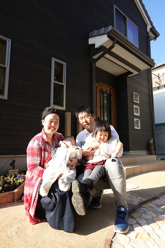 黒っぽい壁の一軒家の玄関の前での家族四人での集合写真