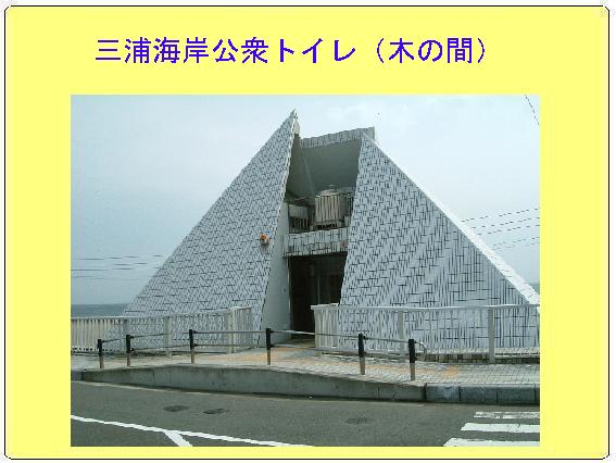 三角形の形状に白い壁の三浦海岸公衆トイレ（木の間）の写真