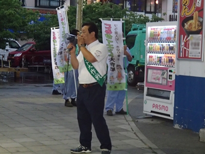 男性がたすきをかけて演説を行なっている街頭キャンペーンの写真