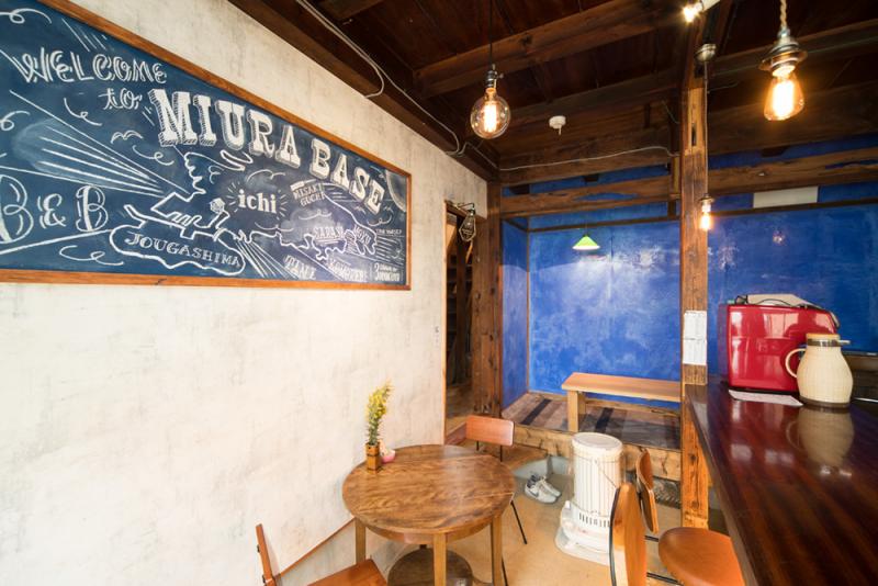 天井からランプが下がり、黒板の飾られた壁の下に2人がけのテーブルがあるbed&breakfast ichiの内装写真