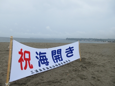 「祝 海開き」の横断幕が砂浜に建てられている写真