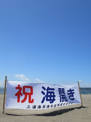 「祝 海開き」の横断幕が地面に立てられている砂浜の写真