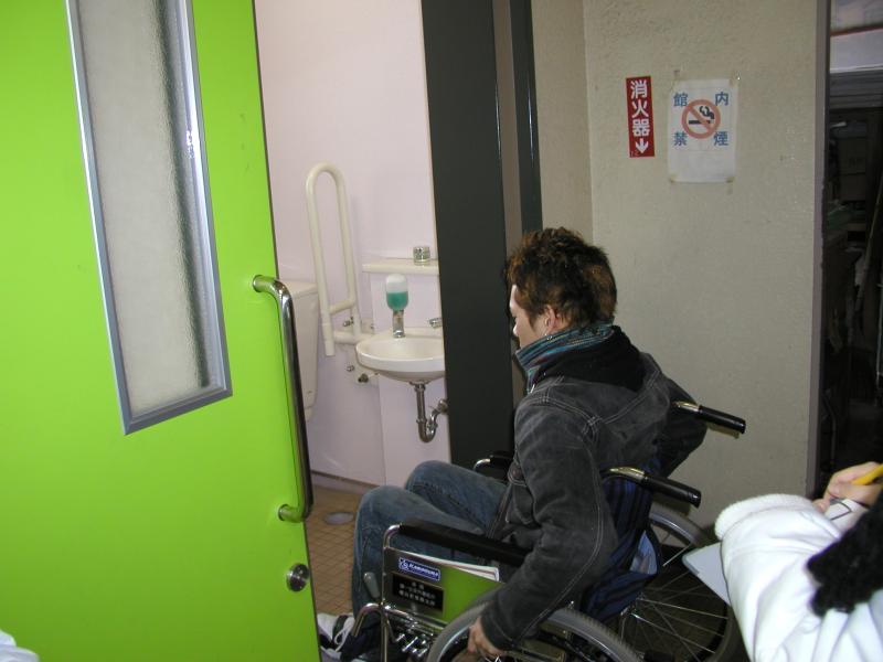 黒いジャンパーを着た車椅子に乗った男性が、半分開かれた黄緑色の横引きのドアから部屋に入る写真
