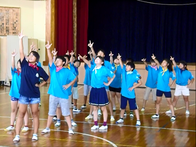 指差すように片手を頭の上に掲げている、三崎小学校の皆さんのダンスの写真