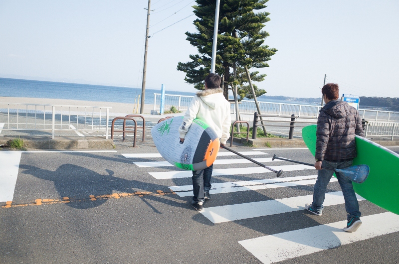 サーフボードを持って横断歩道を渡っている2人の男性の写真