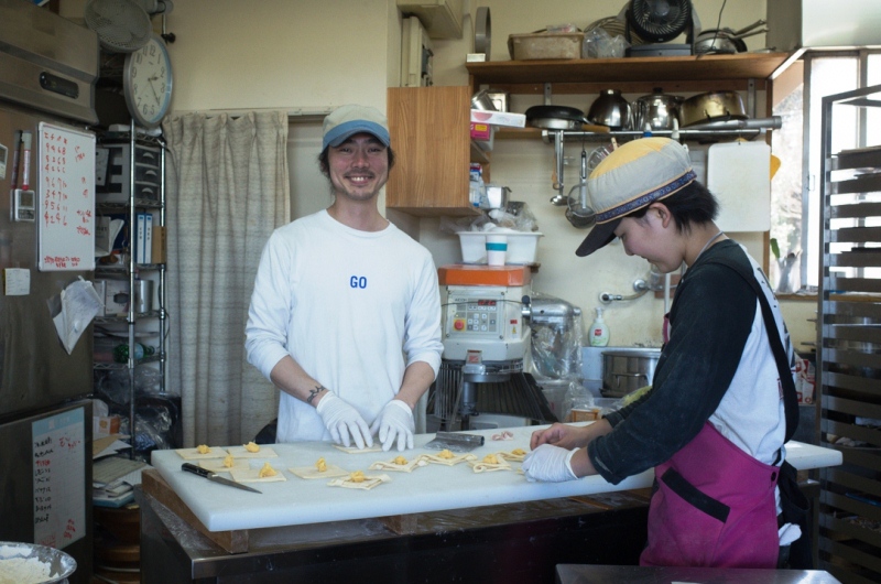 キッチンで向かい合ってパンの成形作業をしている笑顔の男女の写真