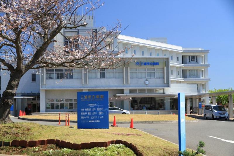 桜の木の向こうに見えている、白い外観の病院の写真