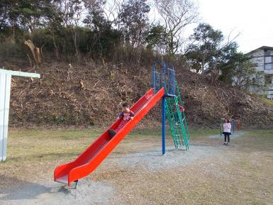 滑る部分が赤色に塗られている滑り台と、滑って遊んでいる子どもの写真